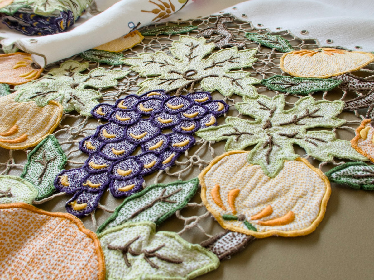 Close view of hand embroidered pumpkins, grapes and vine leaves in Richelieu cutwork on a vintage Madeira tablecloth