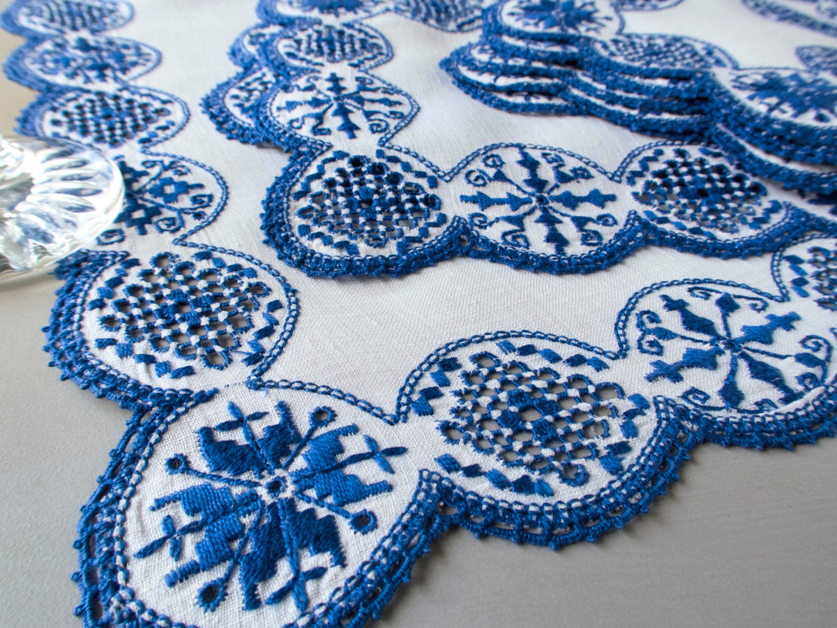 Close-up of vintage Italian white linen with dense cobalt blue geometric medallion embroidery and bold scalloped edges