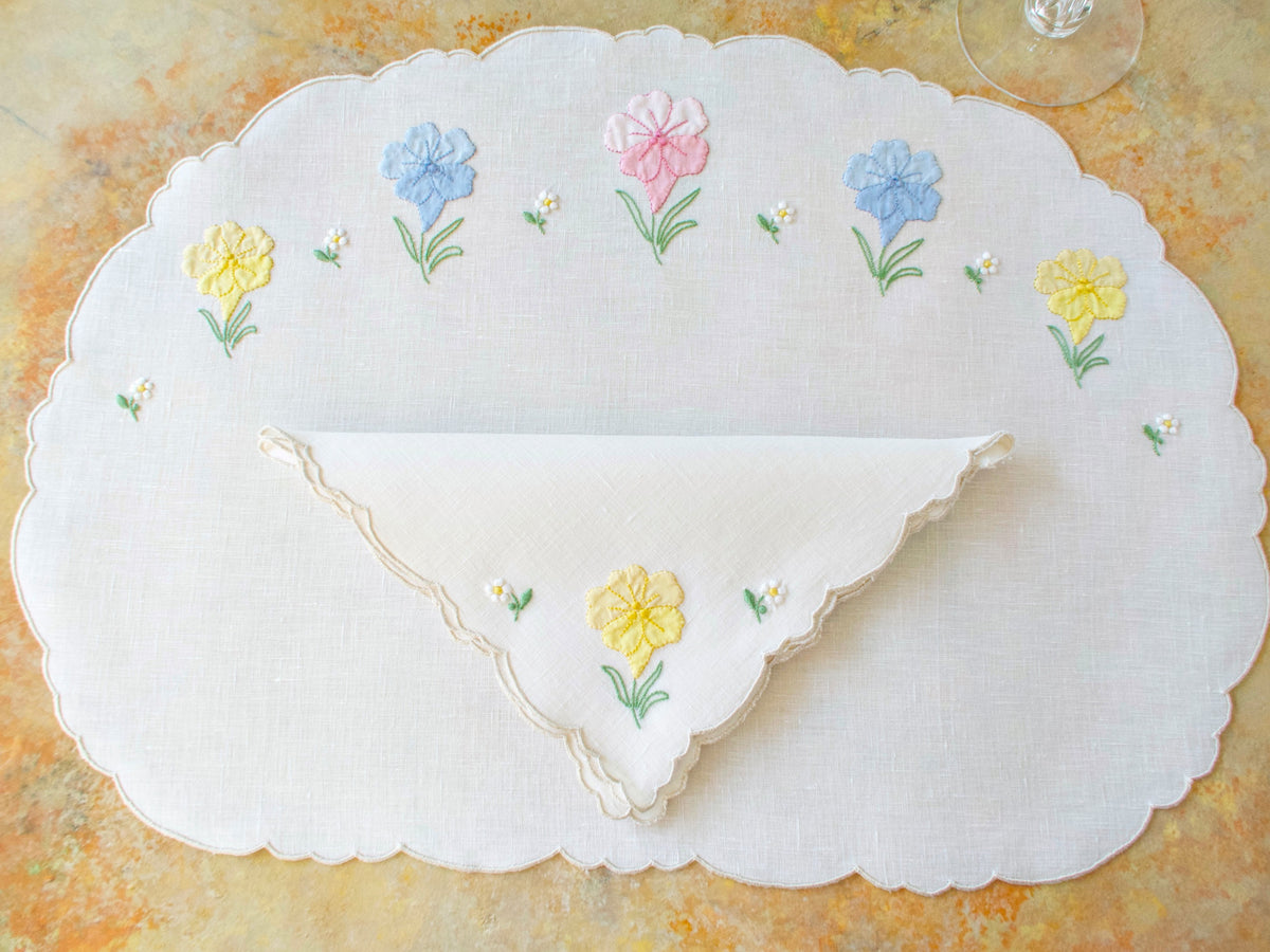 Vintage Madeira oval placemat set for 8 with folded napkin showing spring flower embroidery in pink, blue, and yellow.