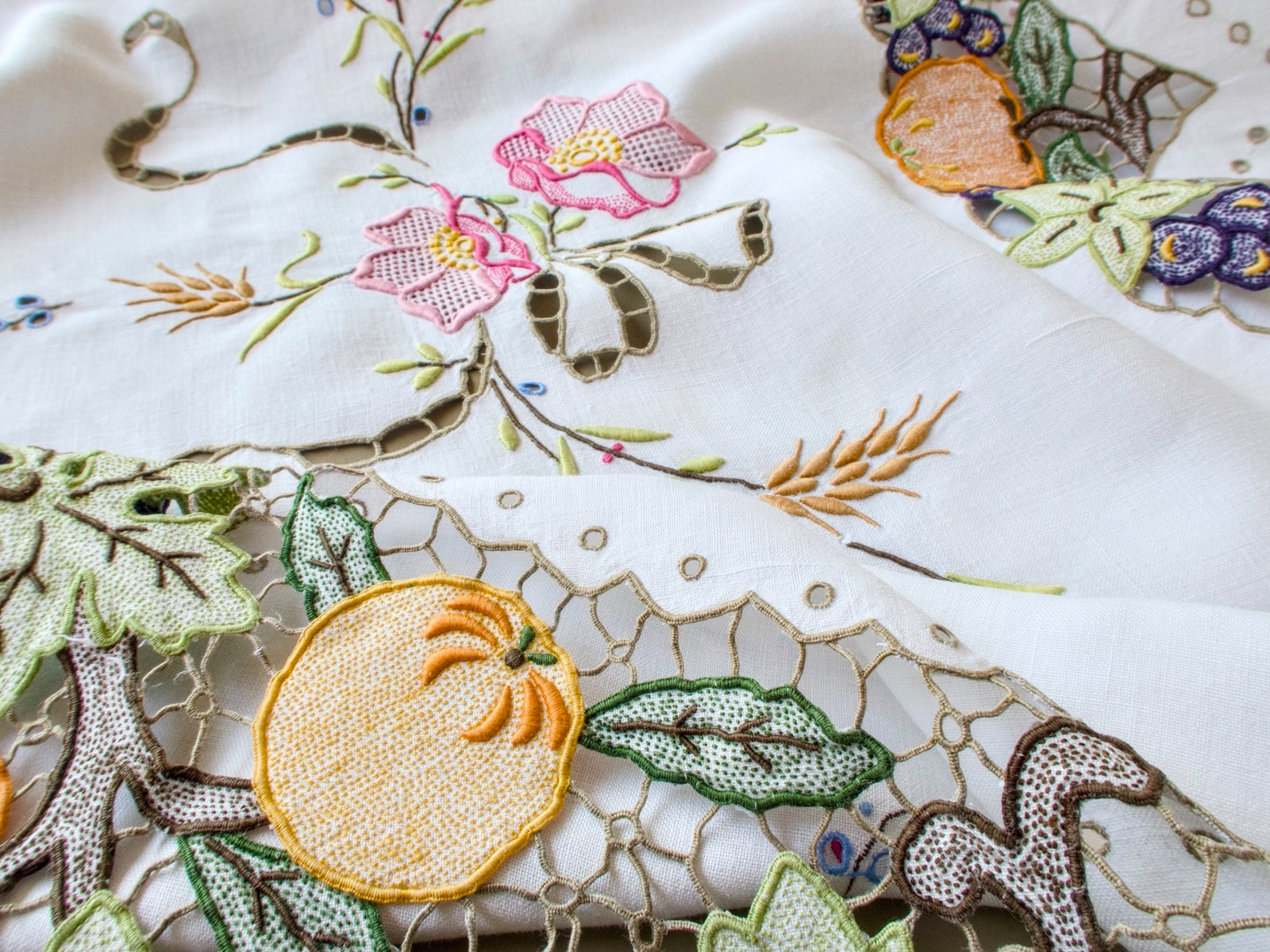 Vintage Madeira tablecloth with blossoms and a cutwork ribbon bow above a corner of Richelieu pumpkins and grapes with an eyelet scalloped edge