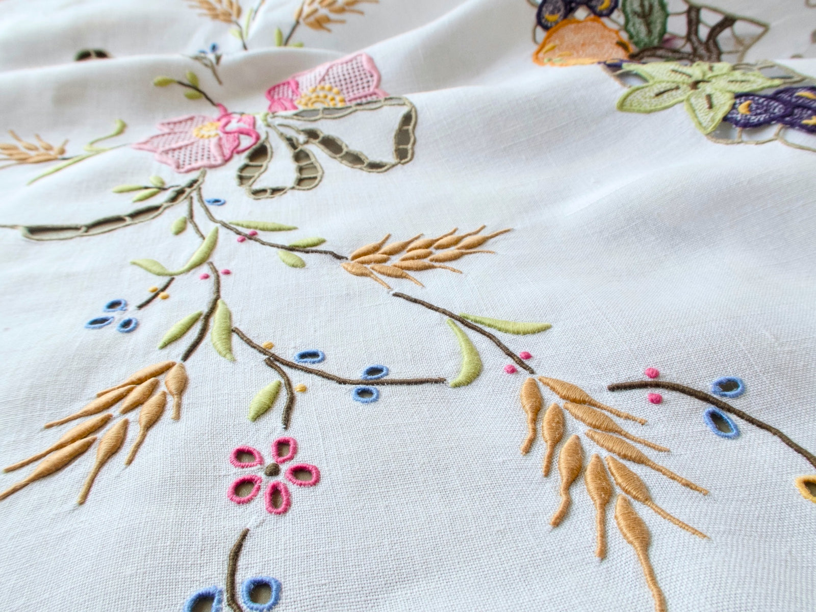 Vintage Madeira tablecloth with blossoms and a cutwork ribbon bow above a corner of Richelieu pumpkins and grapes with an eyelet scalloped edge