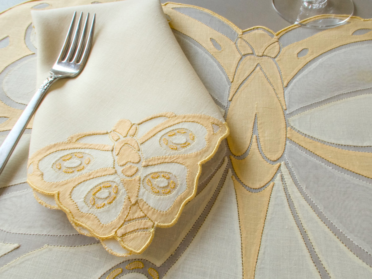 Close-up of vintage Madeira butterfly placemat with fork, showing dimensional wing construction in sheer organdy and linen appliqué on pale yellow ground​​​​​​​​​​​​​​​​