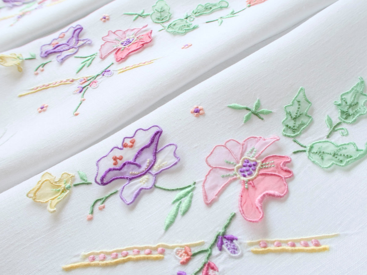 Close-up of vintage Madeira guest towel showing detached organdy trembler petals in pink, purple, and yellow on white Irish linen.