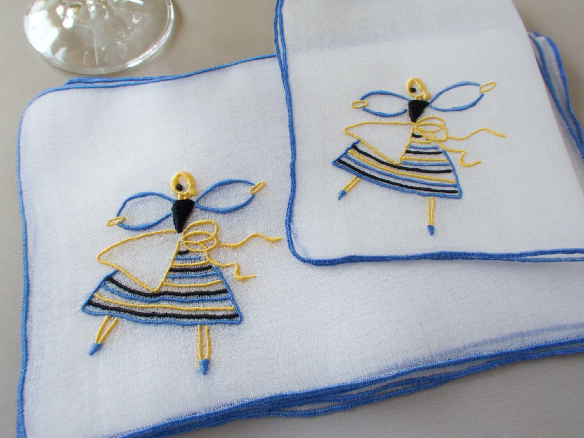 Marghab Dancer cocktail napkins, hand embroidered in yellow, blue, and black on sheer white organdy.