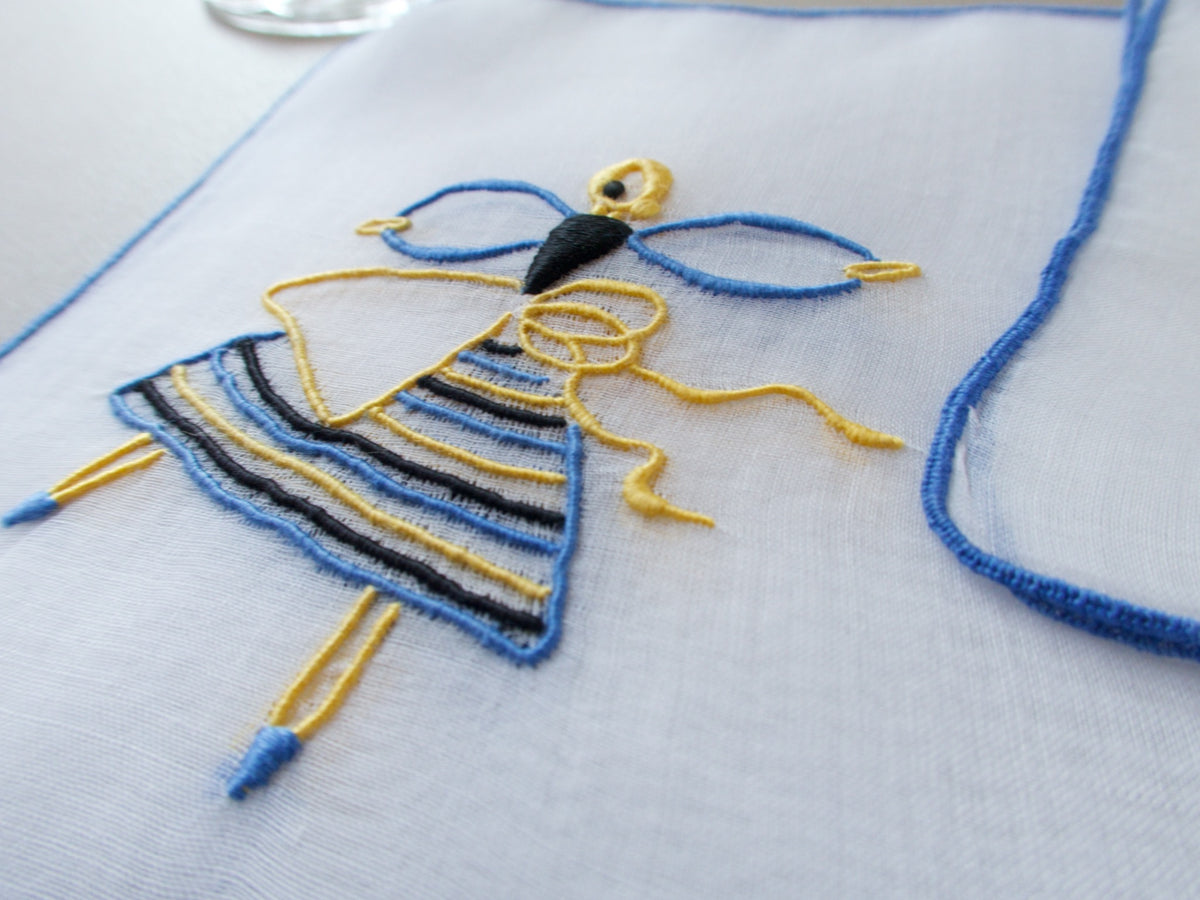 Detail of a Marghab Dancer cocktail napkin, hand embroidered in yellow, blue, and black on sheer white organdy.