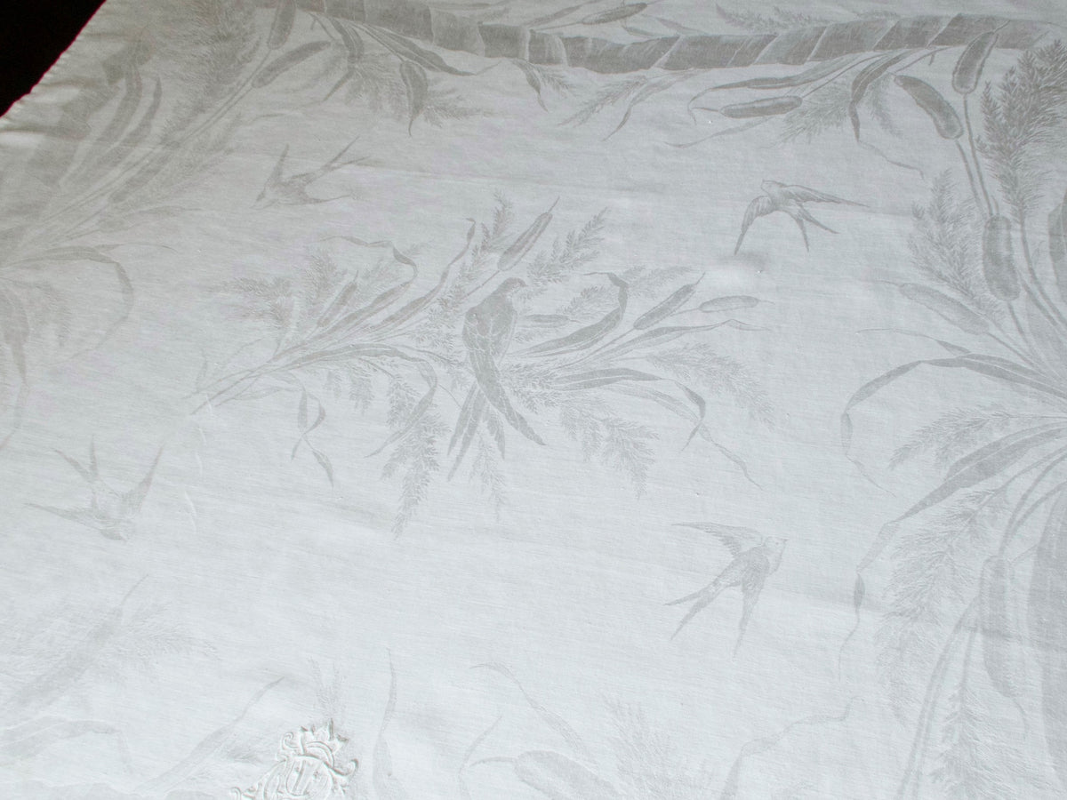 Close view, exposure lowered, of an antique damask linen napkin showing swallows and reeds woven into the pictorial damask weave