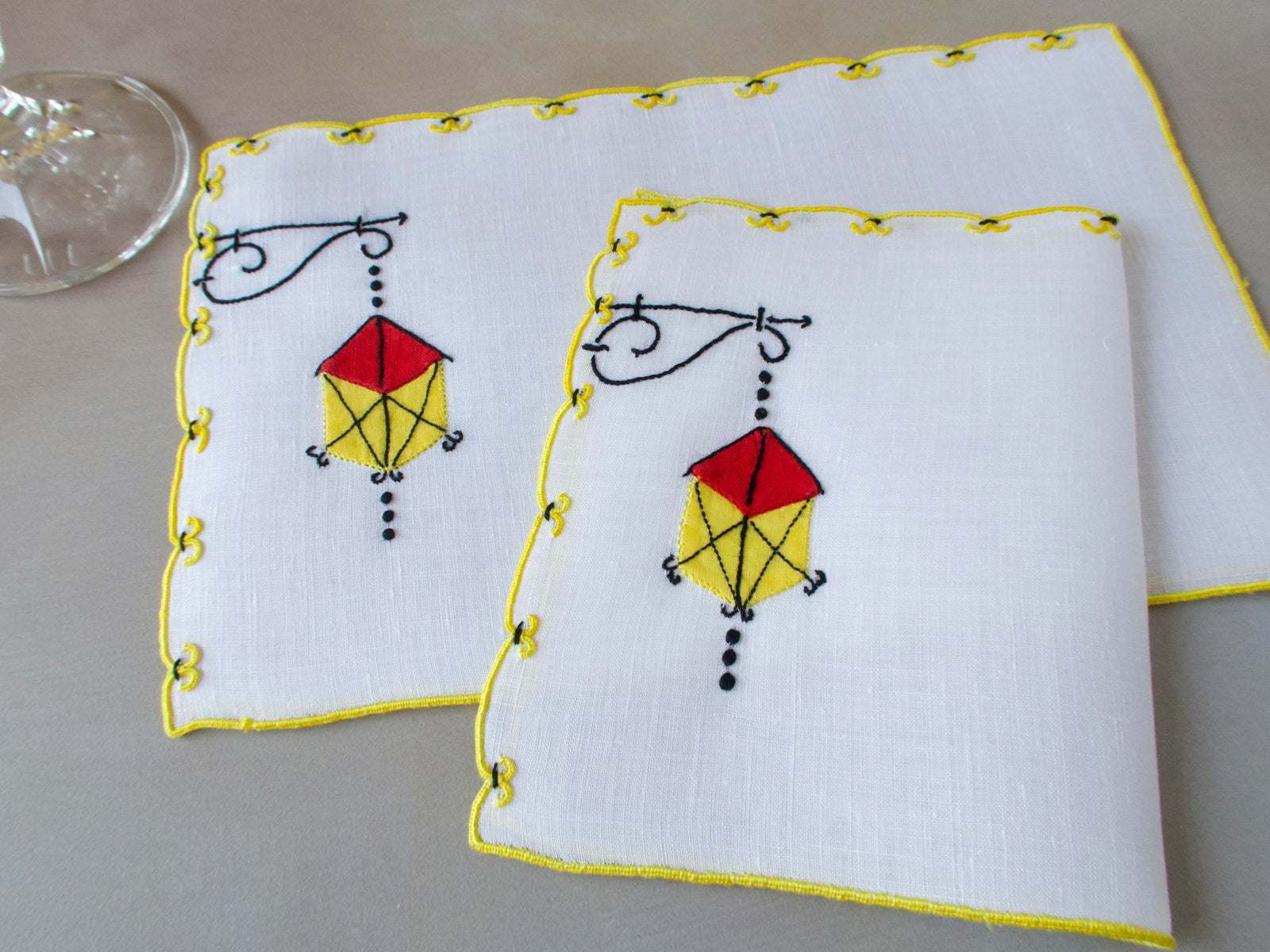 Marghab Lantern cocktail napkins, hand embroidered in red, yellow, and black on white linen with yellow edges.
