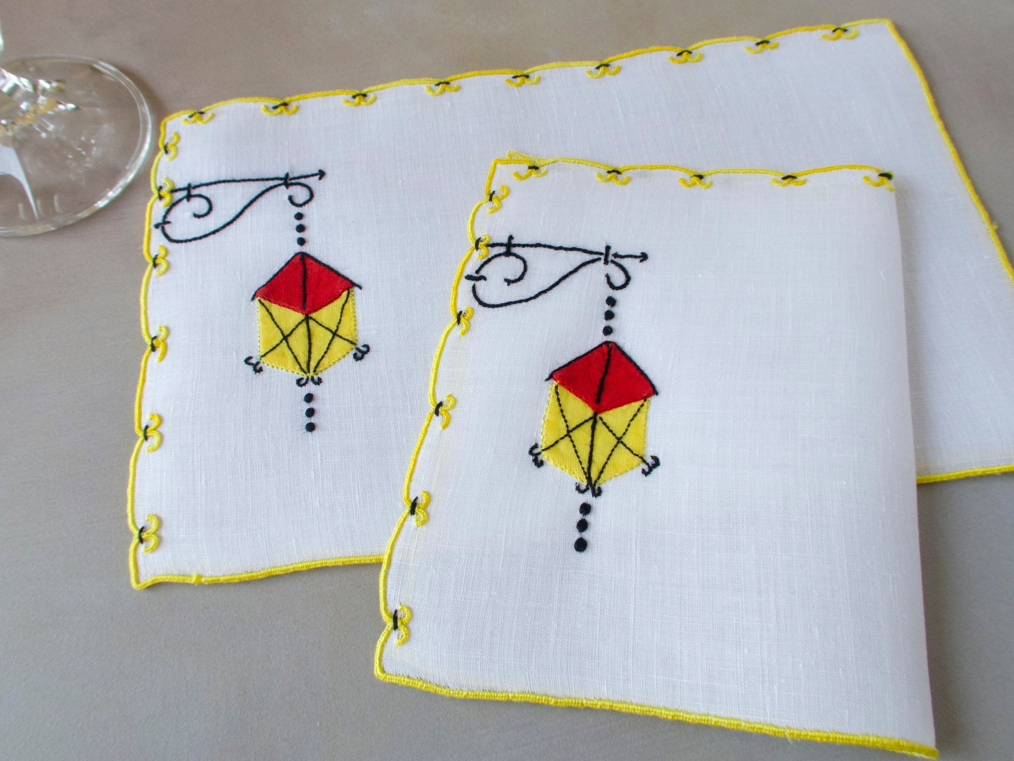 Marghab Lantern cocktail napkins, hand embroidered in red, yellow, and black on white linen with yellow edges.