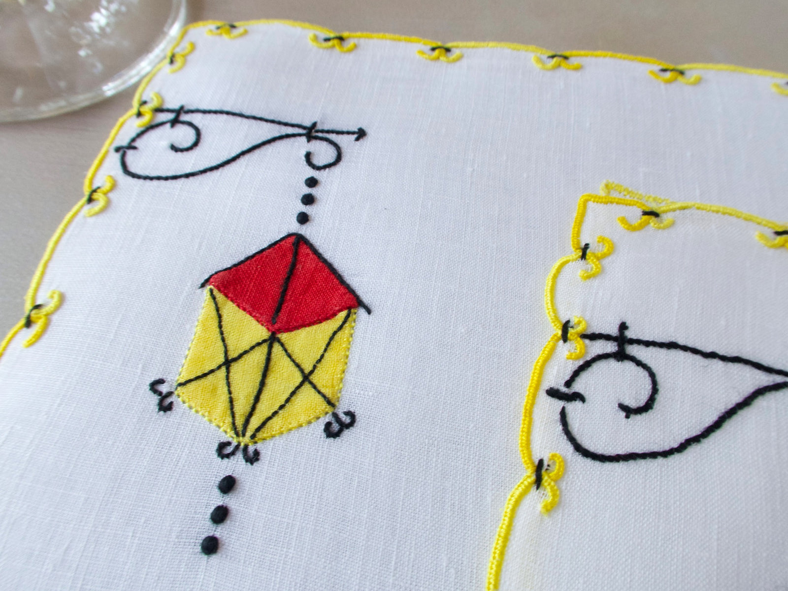 Marghab Lantern cocktail napkins, hand embroidered in red, yellow, and black on white linen with yellow edges.