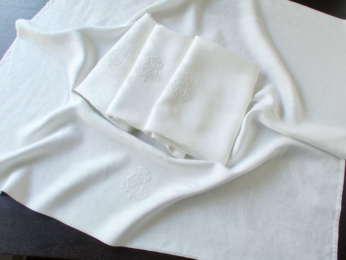 Antique damask linen napkins folded and stacked, one embroidered ACR monogram catching the light