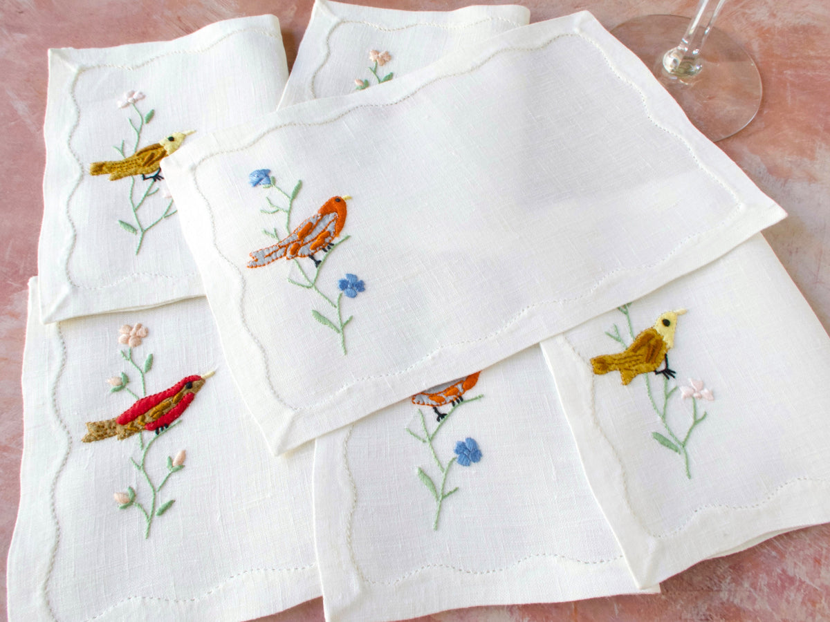 Stack of vintage Madeira linen cocktail napkins with bird and flowering branch embroidery, neatly folded​​​​​​​​​​​​​​​​