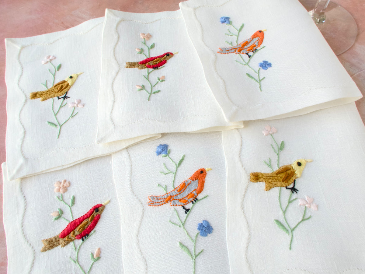 Set of six vintage Madeira embroidered cocktail napkins fanned out, showing colorful bird and floral embroidery on linen
