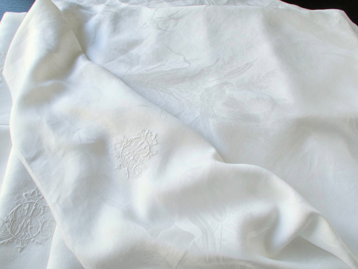 Close view of an antique damask linen napkin showing the woven bird and reed pattern beside the embroidered ACR monogram