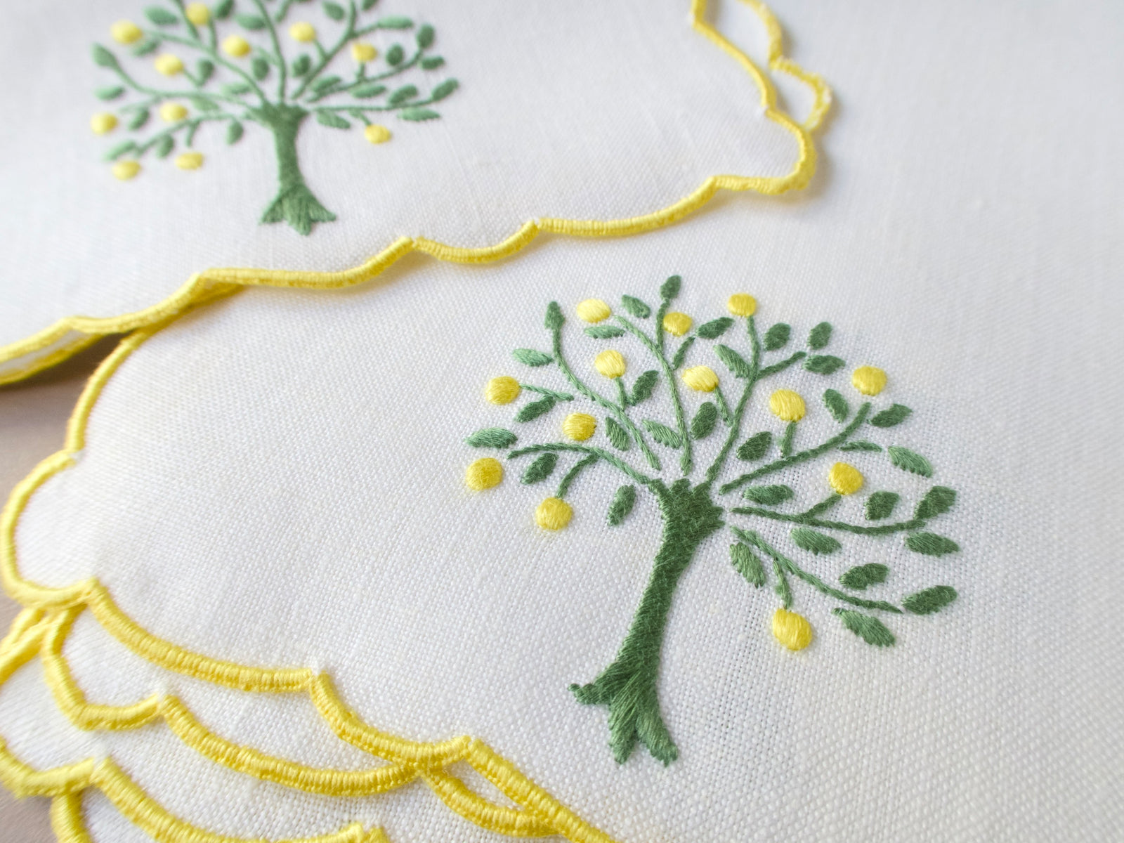 Vintage white linen cocktail napkin hand embroidered in Madeira with a lemon tree in green and yellow, finished with scalloped yellow edges