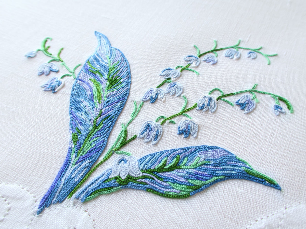 Detail of D. Porthault Lily of the Valley embroidery showing deep blue leaf shading and white bell flowers in Point de Beauvais stitch.