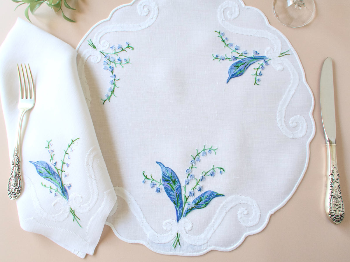Vintage D. Porthault round placemat set for 10 with napkin and silverware showing full place setting and scalloped edge detail.