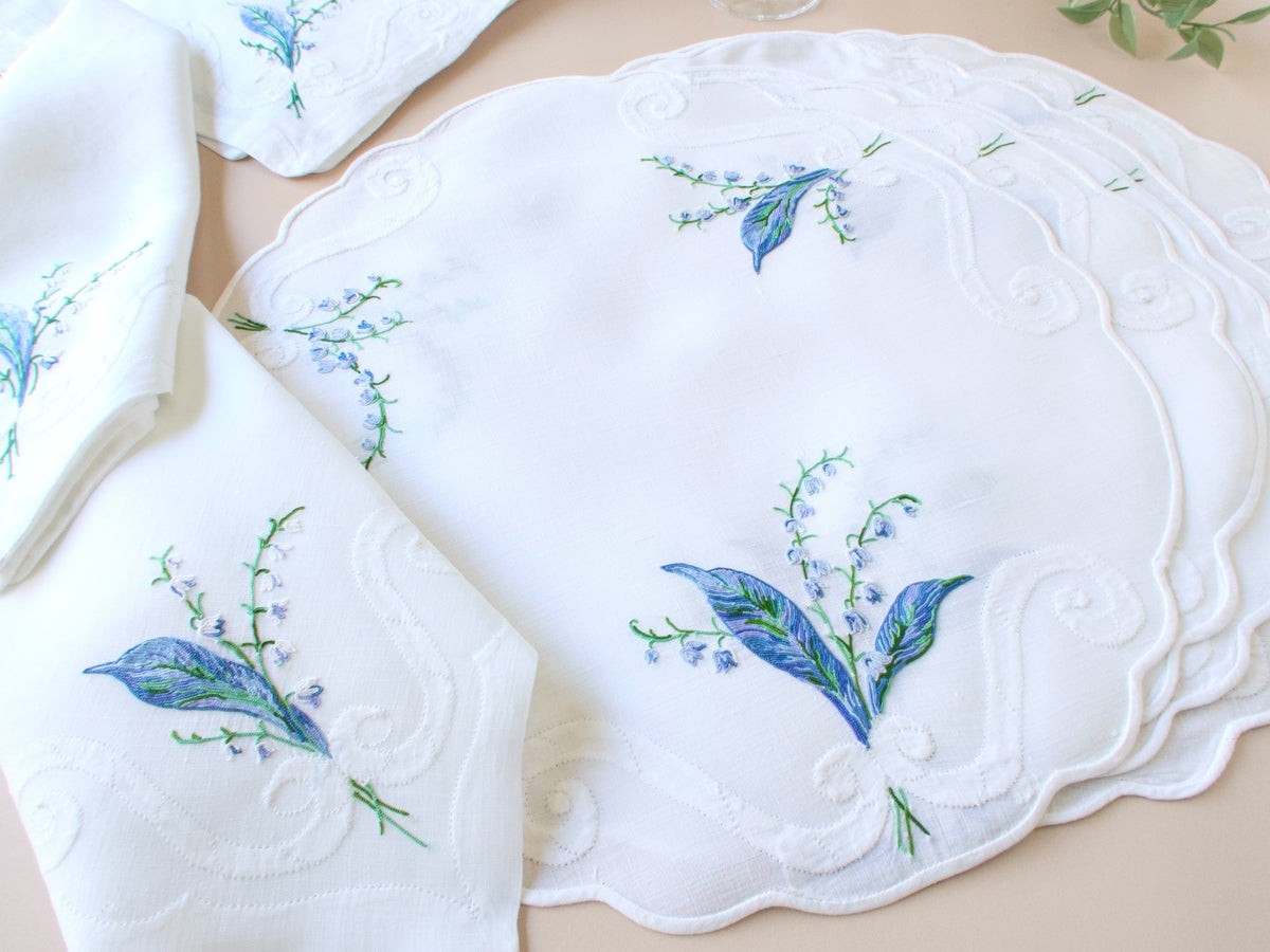 Stacked vintage D. Porthault round linen placemats showing full Lily of the Valley motif and scalloped edge on white ground.