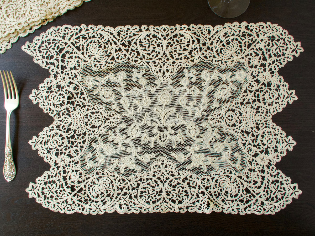 Whole antique lace placemat with pointed bobbin lace sides and a Milanese lace center beside a fork and wine glass