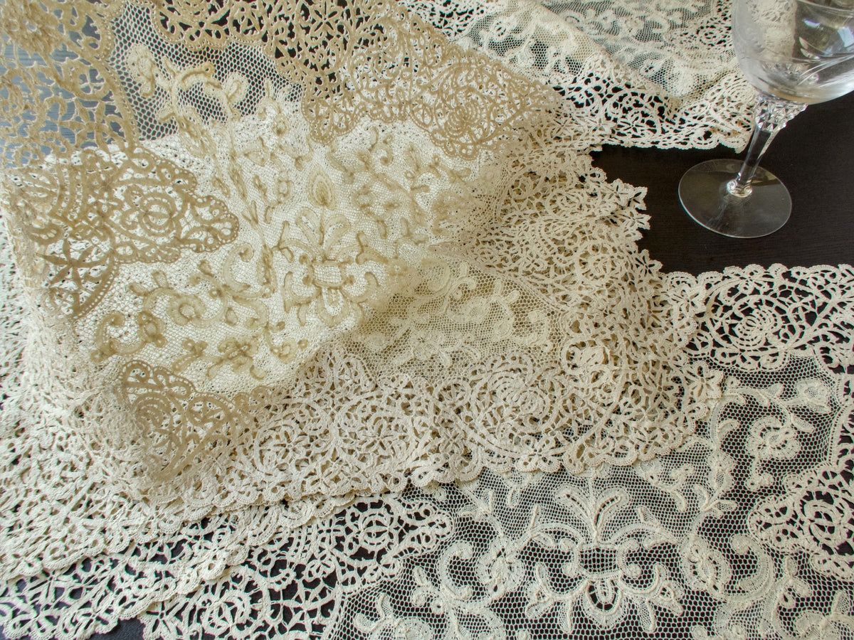 Antique lace placemats layered together beside a wine glass, the airy sheer net and openwork showing through
