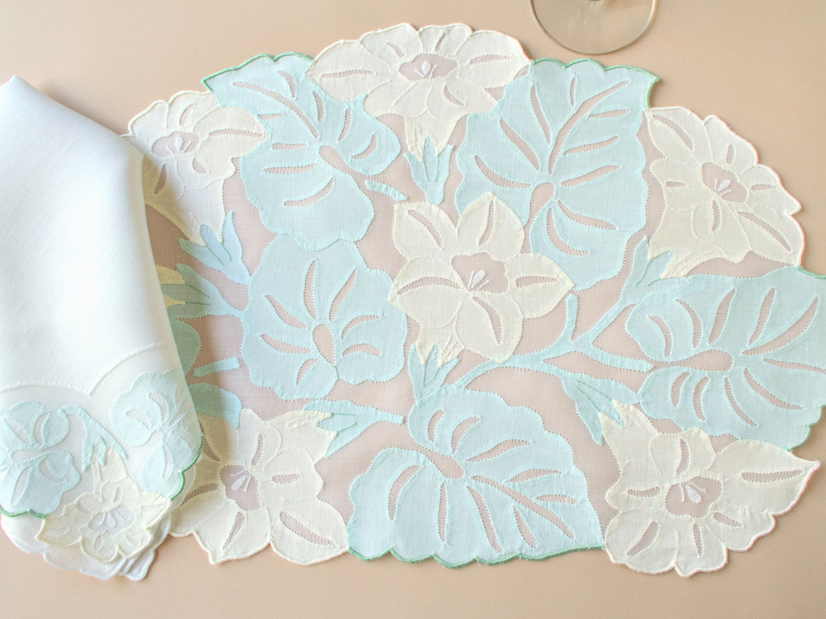Vintage Madeira organdy placemat folded with linen napkin showing scalloped leaf-shaped edge and pastel embroidered floral detail.