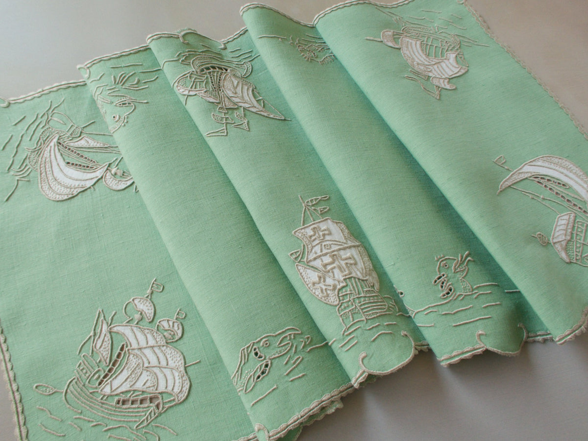 Vintage Marghab “Old Ships” placemat and napkin set, hand embroidered in Madeira on fine Irish linen in sea-green tones, featuring ships, waves, and mythical sea creatures in intricate raised embroidery.