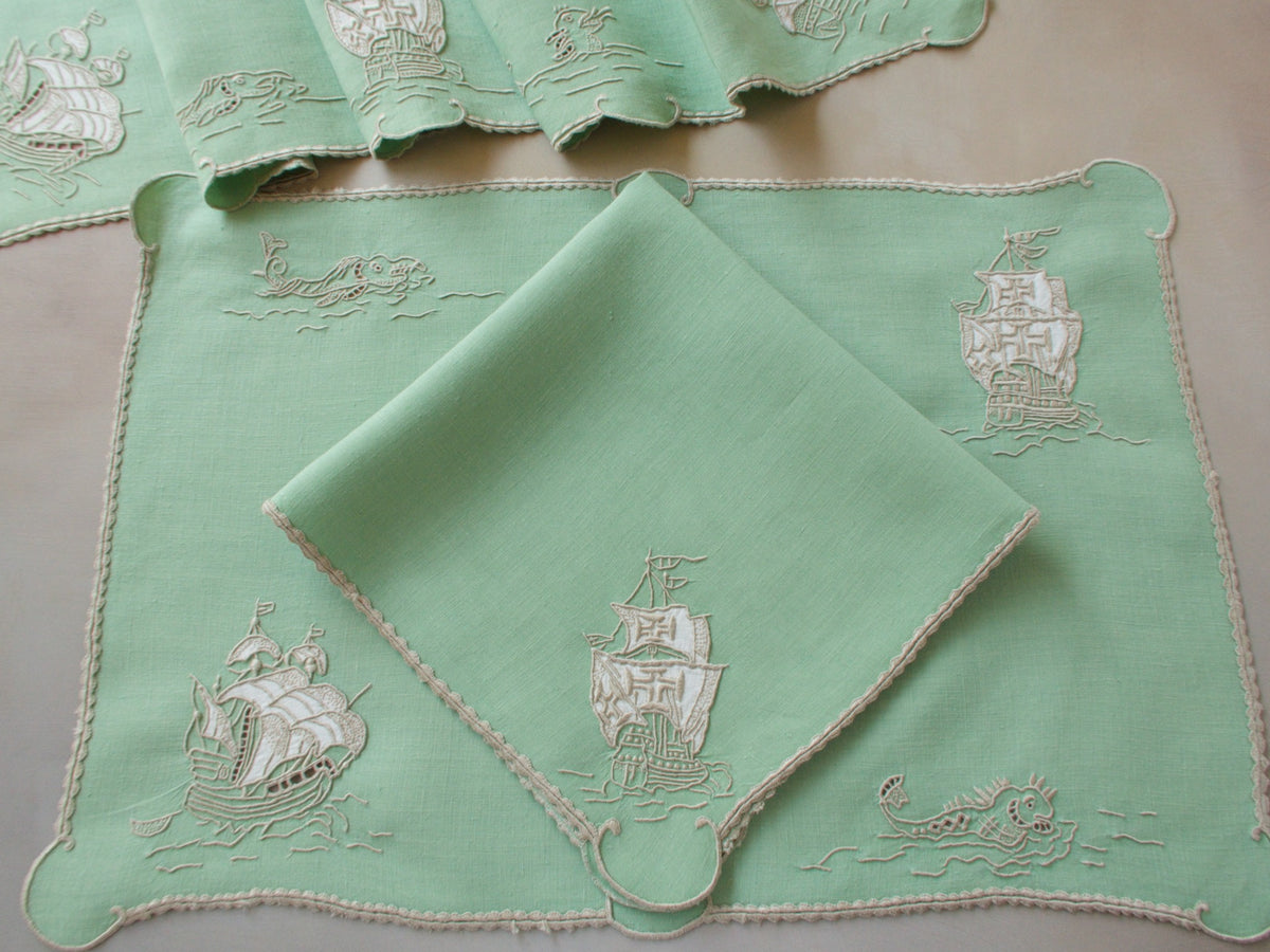 Vintage Marghab “Old Ships” placemat and napkin set, hand embroidered in Madeira on fine Irish linen in sea-green tones, featuring ships, waves, and mythical sea creatures in intricate raised embroidery.