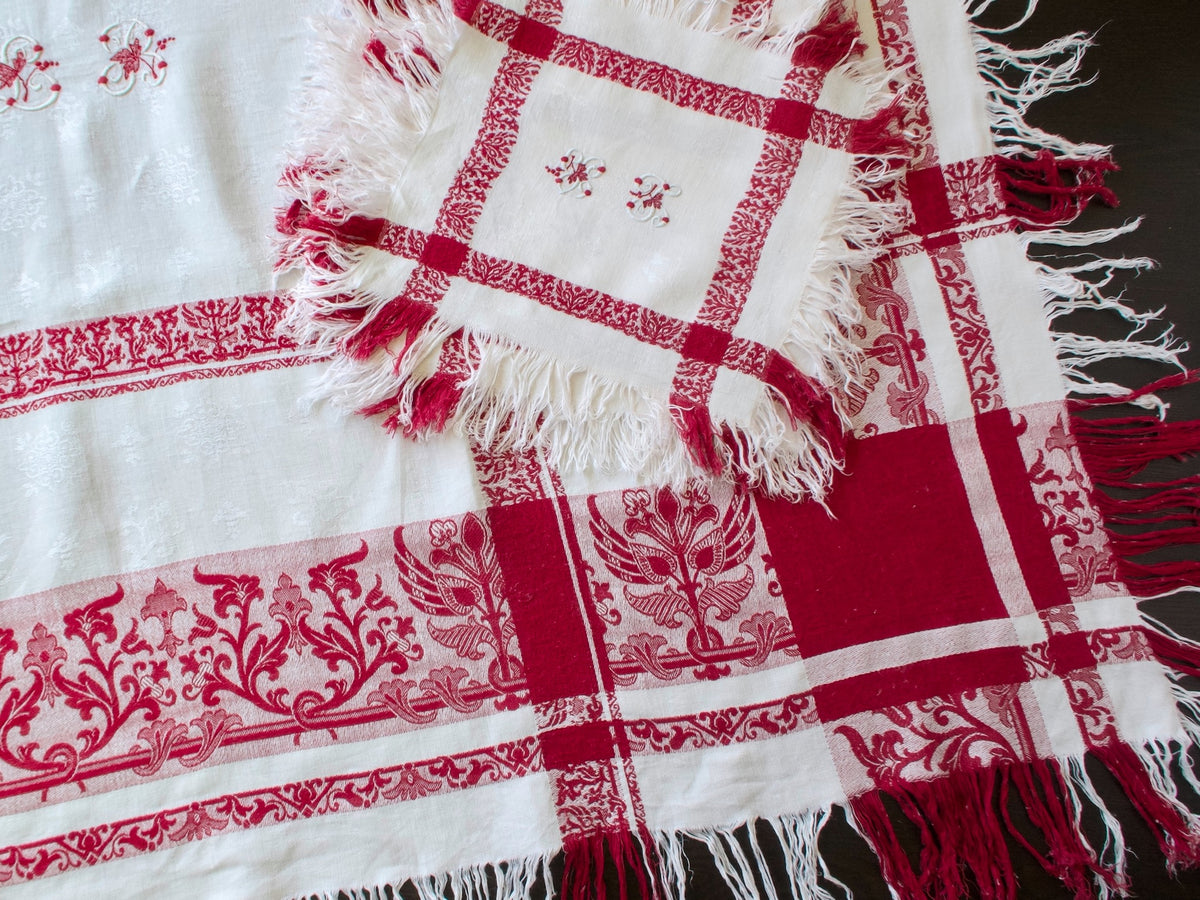 Close-up of the tablecloth and napkin, showing the woven red borders, LB monograms and red and white fringe.
