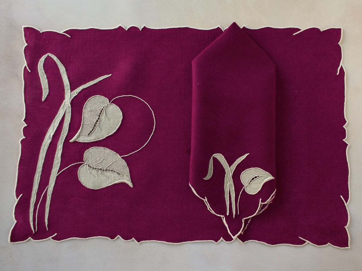 Marghab “Waterleaf” placemat and napkin set in deep plum linen, hand embroidered in Madeira with gray appliqué leaf design.