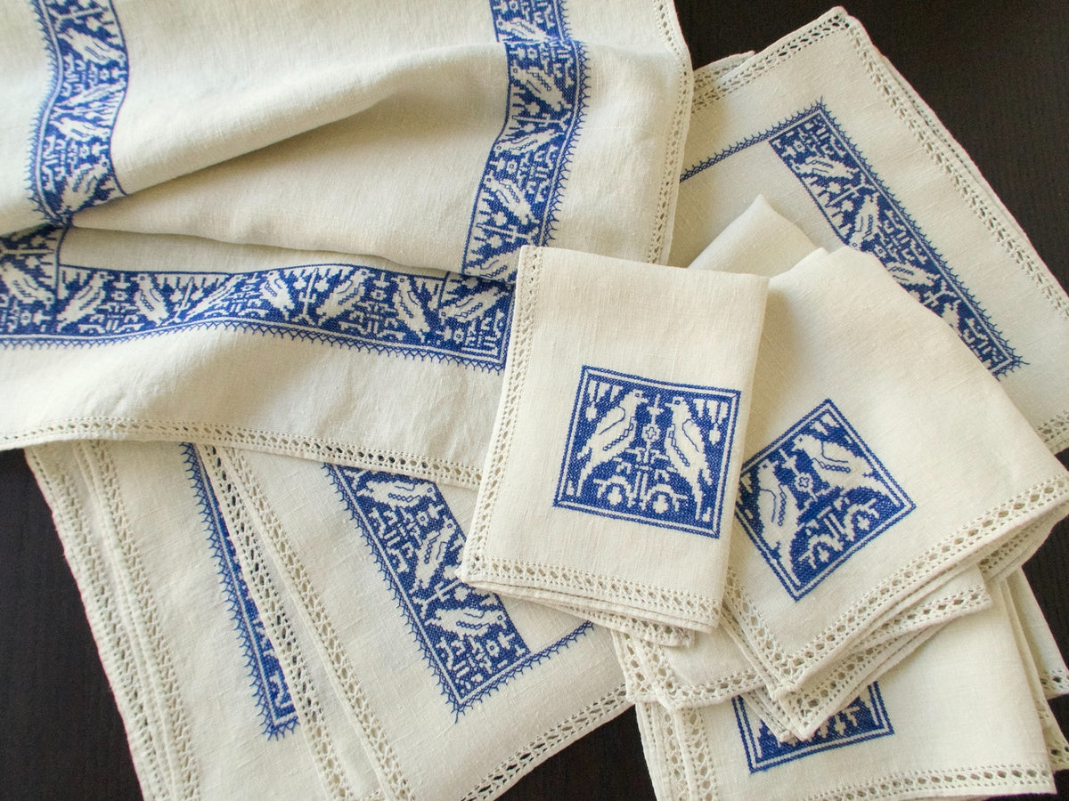 Group of natural linen placemats and napkins with blue Assisi embroidery and drawnwork edges.