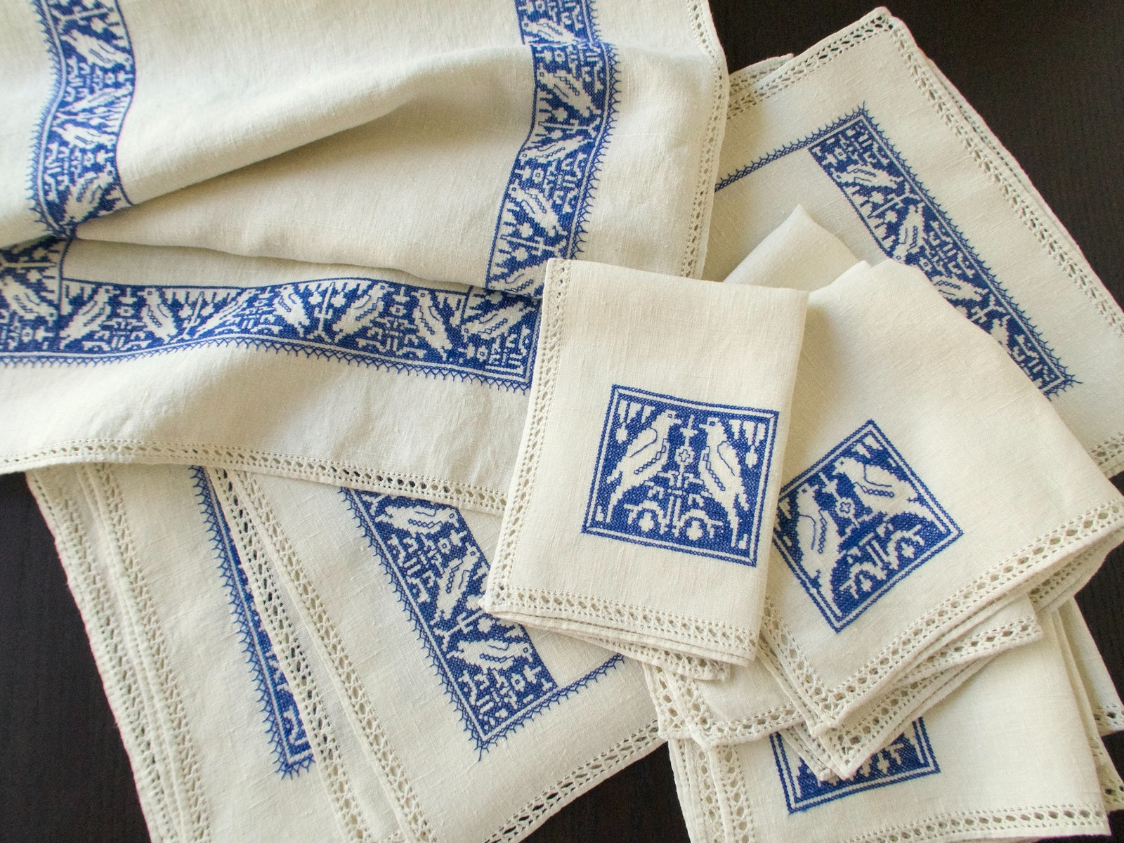 Group of natural linen placemats and napkins with blue Assisi embroidery and drawnwork edges.