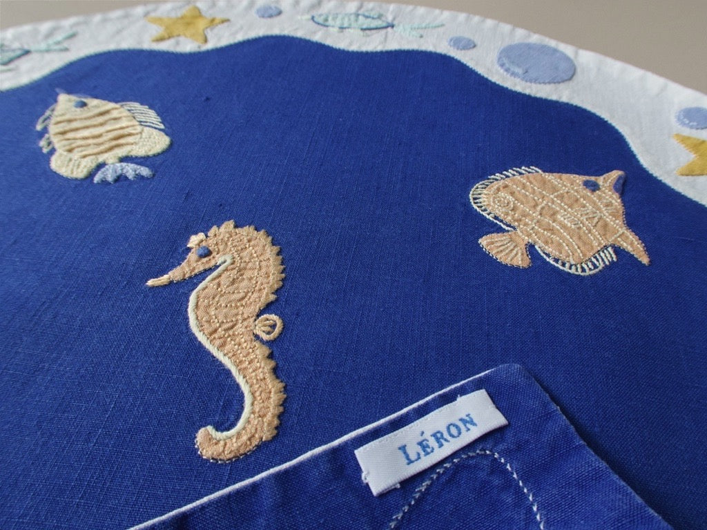 Léron label on vintage deep blue linen placemat, hand embroidered sea creatures visible.​​​​​​​​​​​​​​​​