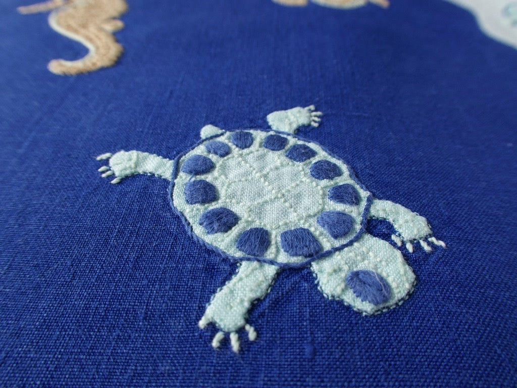 Close view of hand embroidered turtle on vintage Léron deep blue linen placemat, with seahorse and starfish detail.
