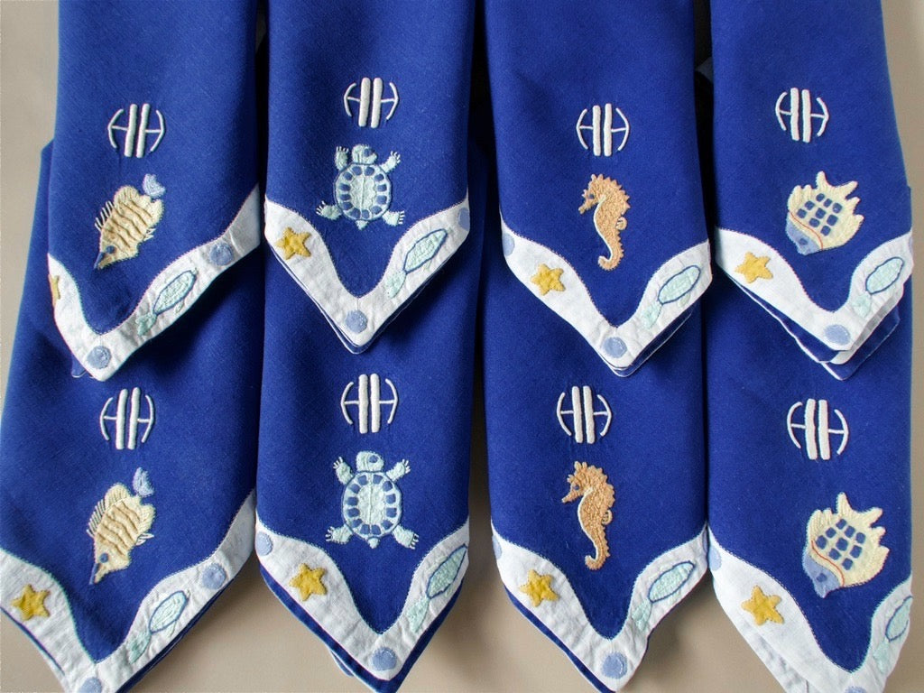 Stack of vintage Léron monogrammed napkins with hand embroidered sea creature border detail.