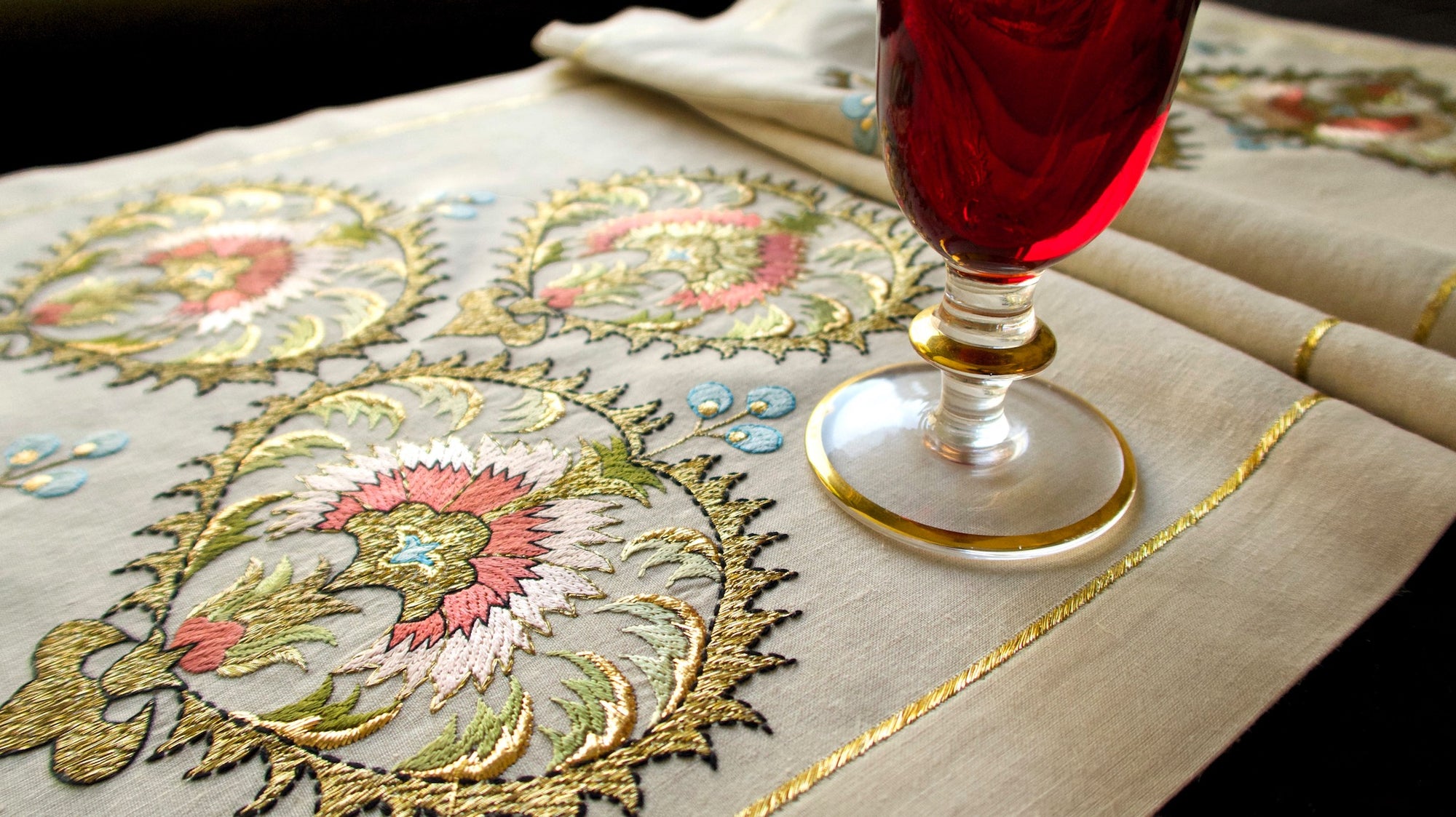 Exquisite vintage linen table runner embroidered in metallic gold, styled with a red glass.