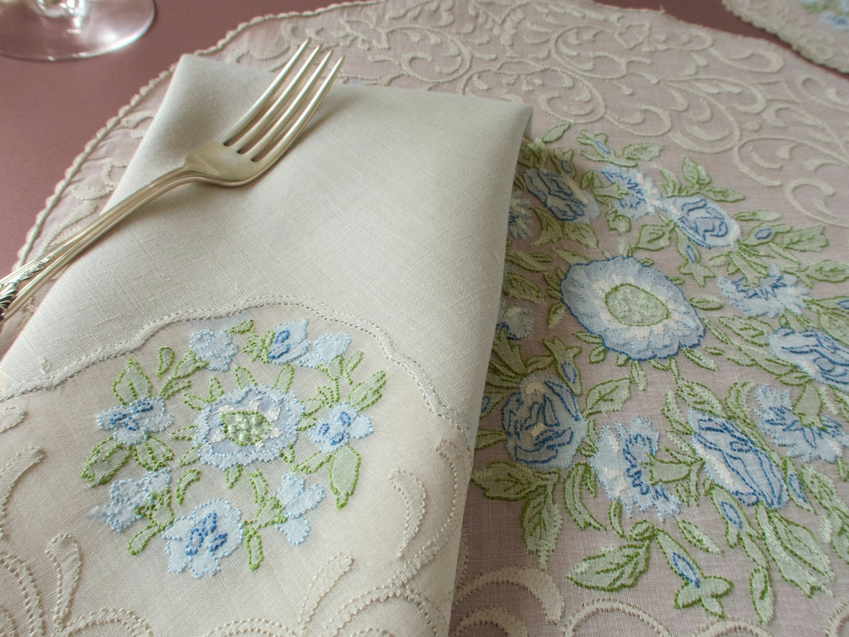 Close up of folded linen napkin and Madeira organdy placemat, blue flower and scrolling motif shadow work embroidery