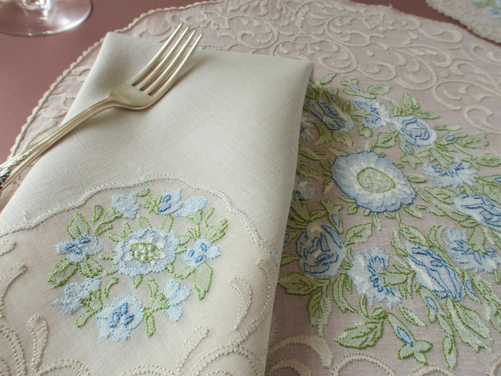 Close up of folded linen napkin and Madeira organdy placemat, blue flower and scrolling motif shadow work embroidery