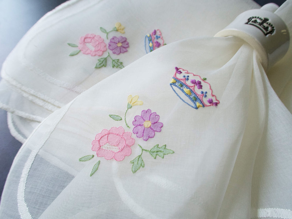 Detail of vintage Italian organdy napkin embroidery showing pastel coronet with pink, yellow, blue, and lavender threads.