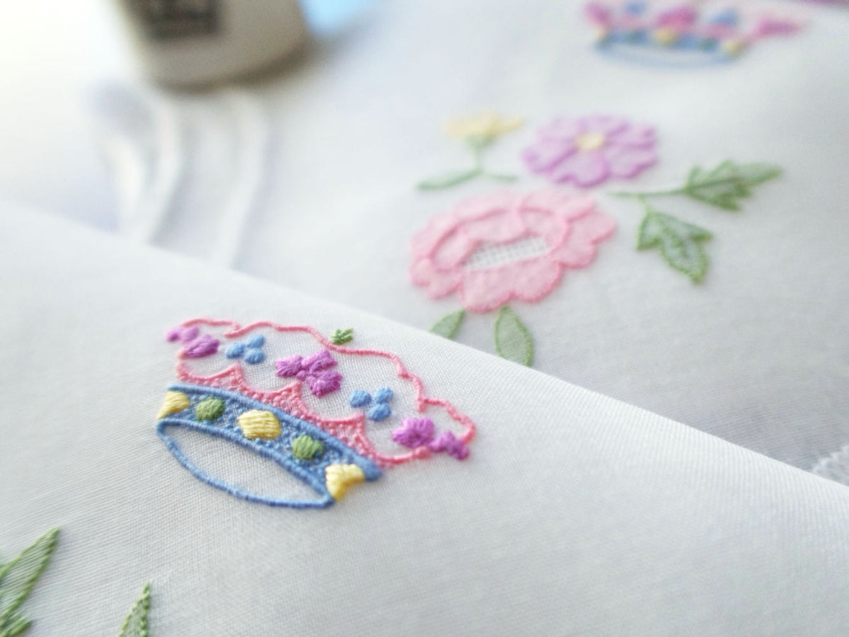 Italian organdy napkin hand embroidered with a colorful coronet and pastel flowers in shadow work, from a vintage 12-piece set.
