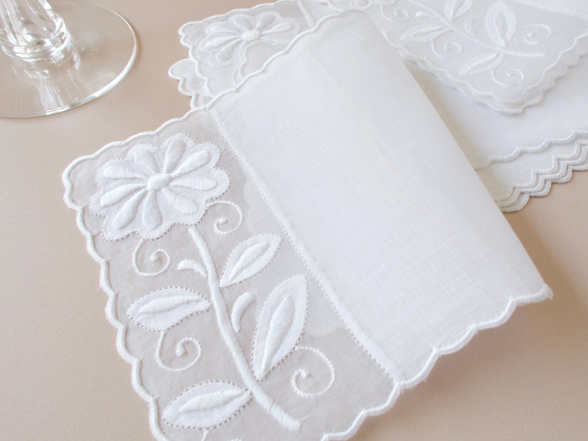 Vintage Madeira white appliqué daisy cocktail napkins on organdy and linen with deeply scalloped edges, stacked with wine glass on beige background.