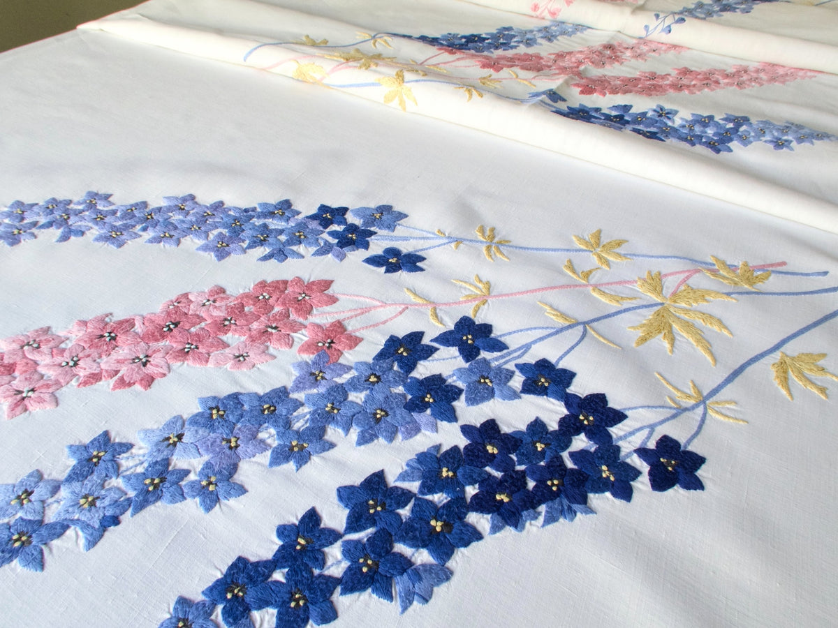 Close-up of vintage hand embroidered blue delphinium flowers on French linen tablecloth