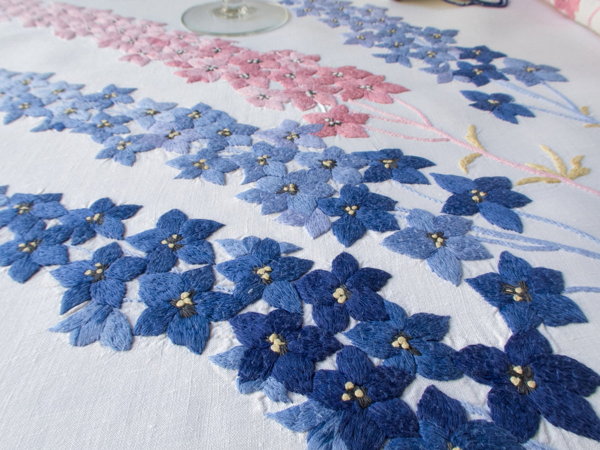 Detail of vintage hand embroidered blue delphinium motifs on French embroidered tablecloth