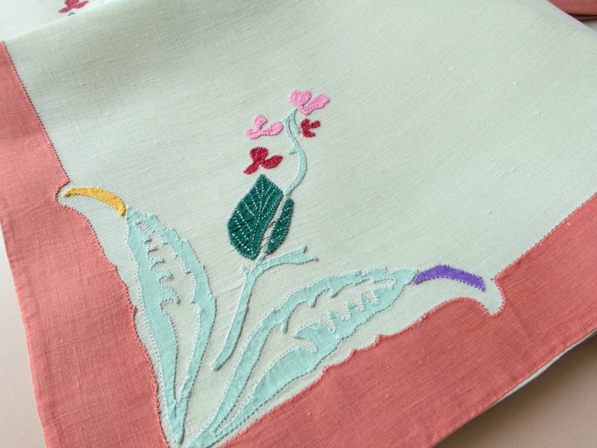Detail of stylized floral appliqué on sage linen napkin, warm coral border, mid-century French