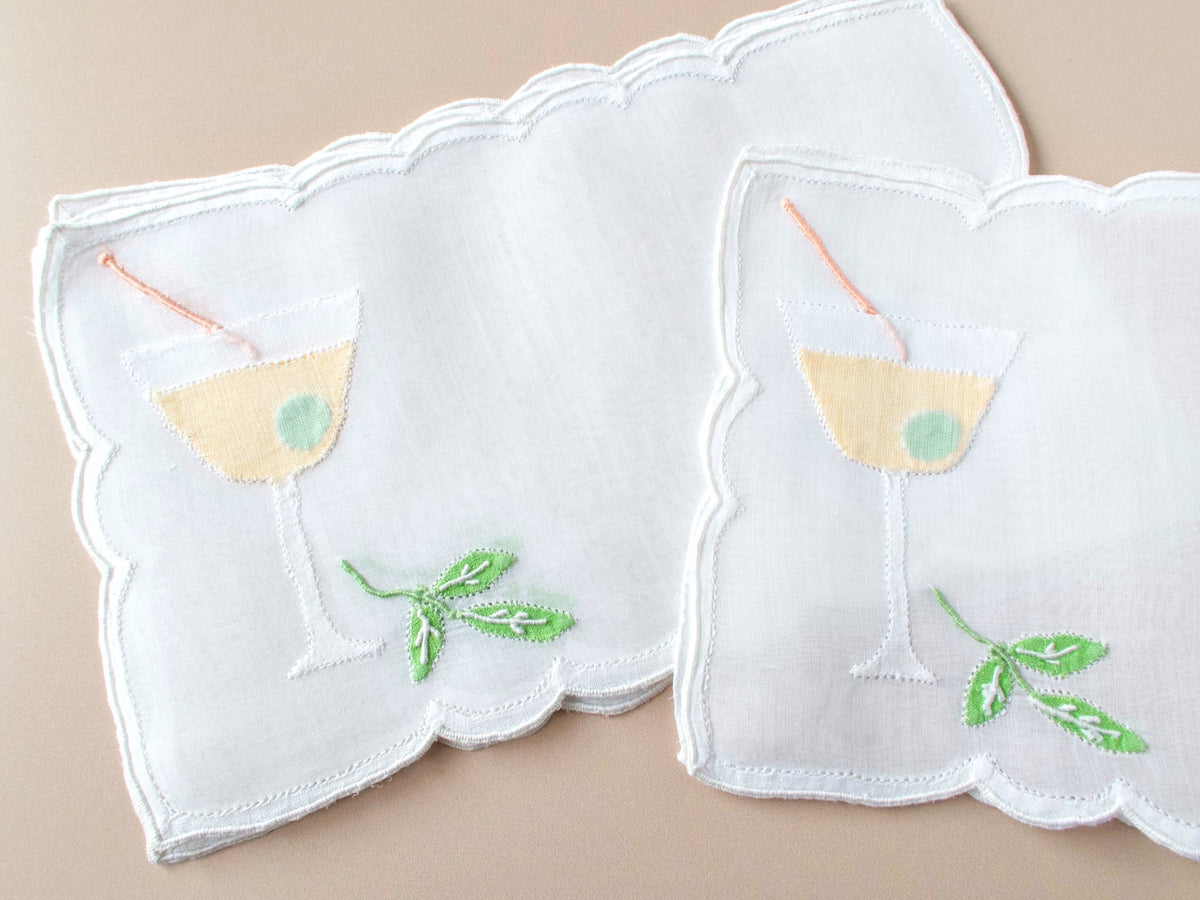 Vintage Madeira organdy cocktail napkins on beige background, two napkins showing martini glass appliqué with olive and embroidered mint sprig.
