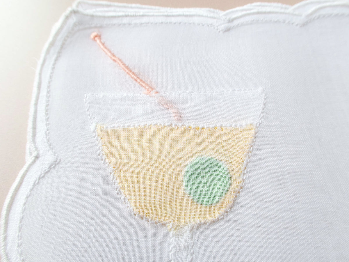 Close-up of vintage Madeira organdy cocktail napkin martini glass with sheer organdy olive overlay and embroidered cocktail pick detail.​​​​​​​​​​​​​​​​