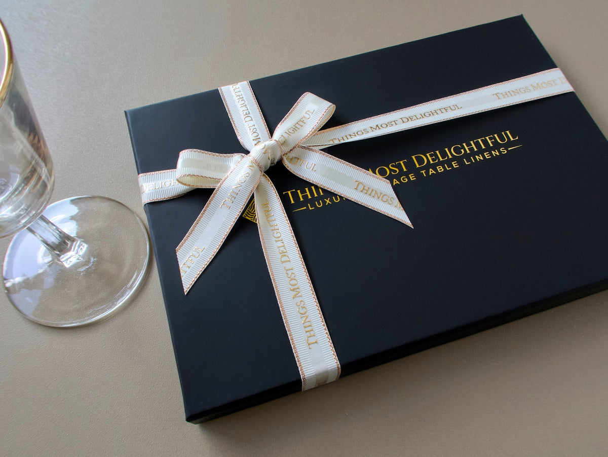 Things Most Delightful gift box tied with ribbon beside a cocktail glass