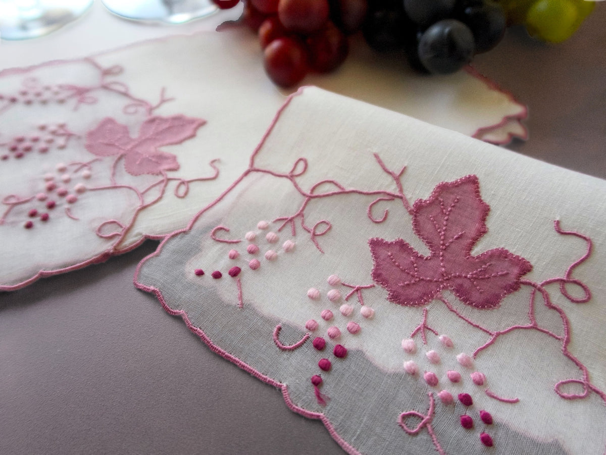 Vintage Madeira cocktail napkins on beige background showing two napkins with organdy window inset and raised pink grape cluster and leaf embroidery with scrolling vines.