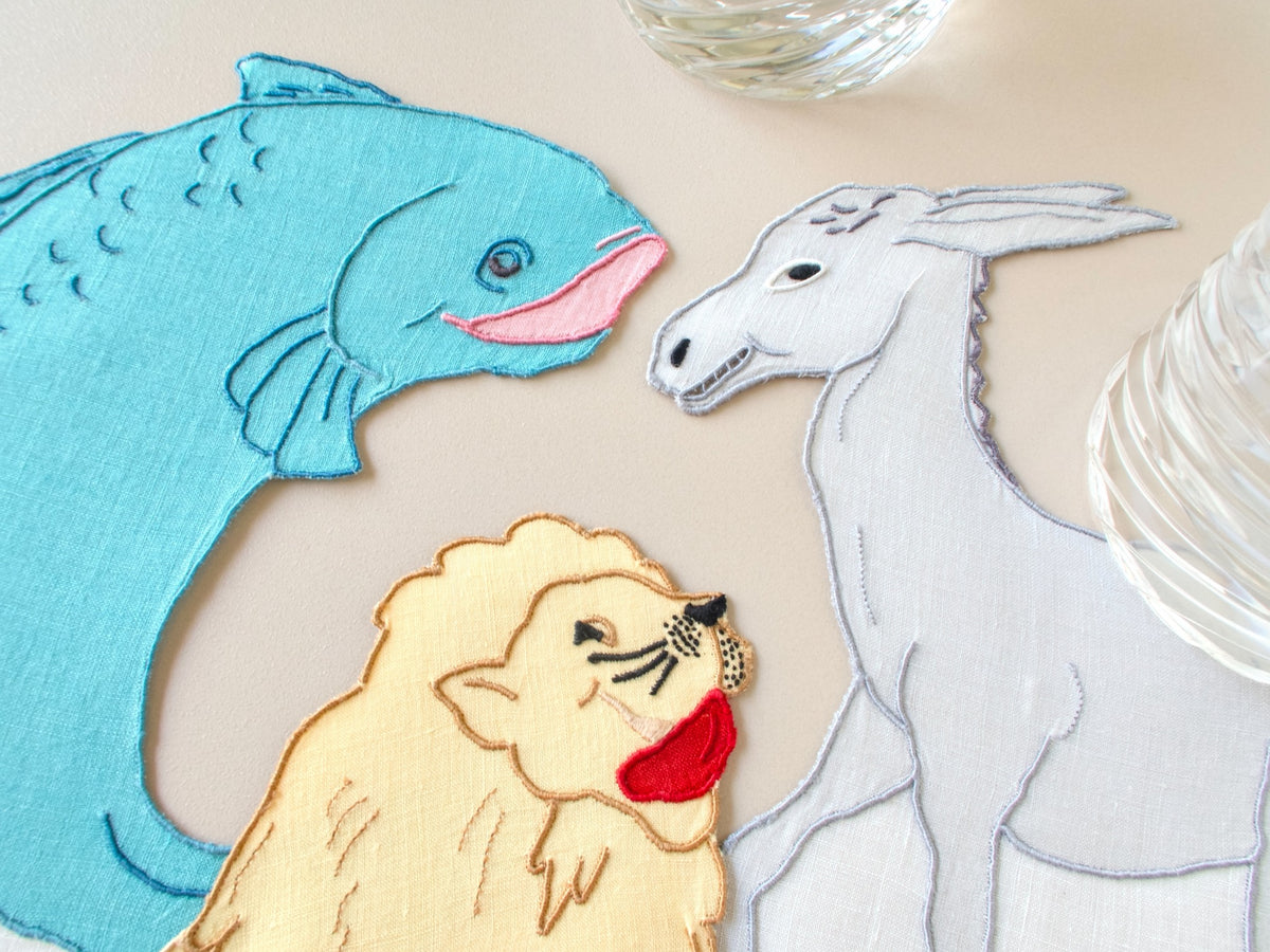 Vintage Madeira hand embroidered cocktail napkins styled on table, fish, donkey and lion silhouettes in colored linen