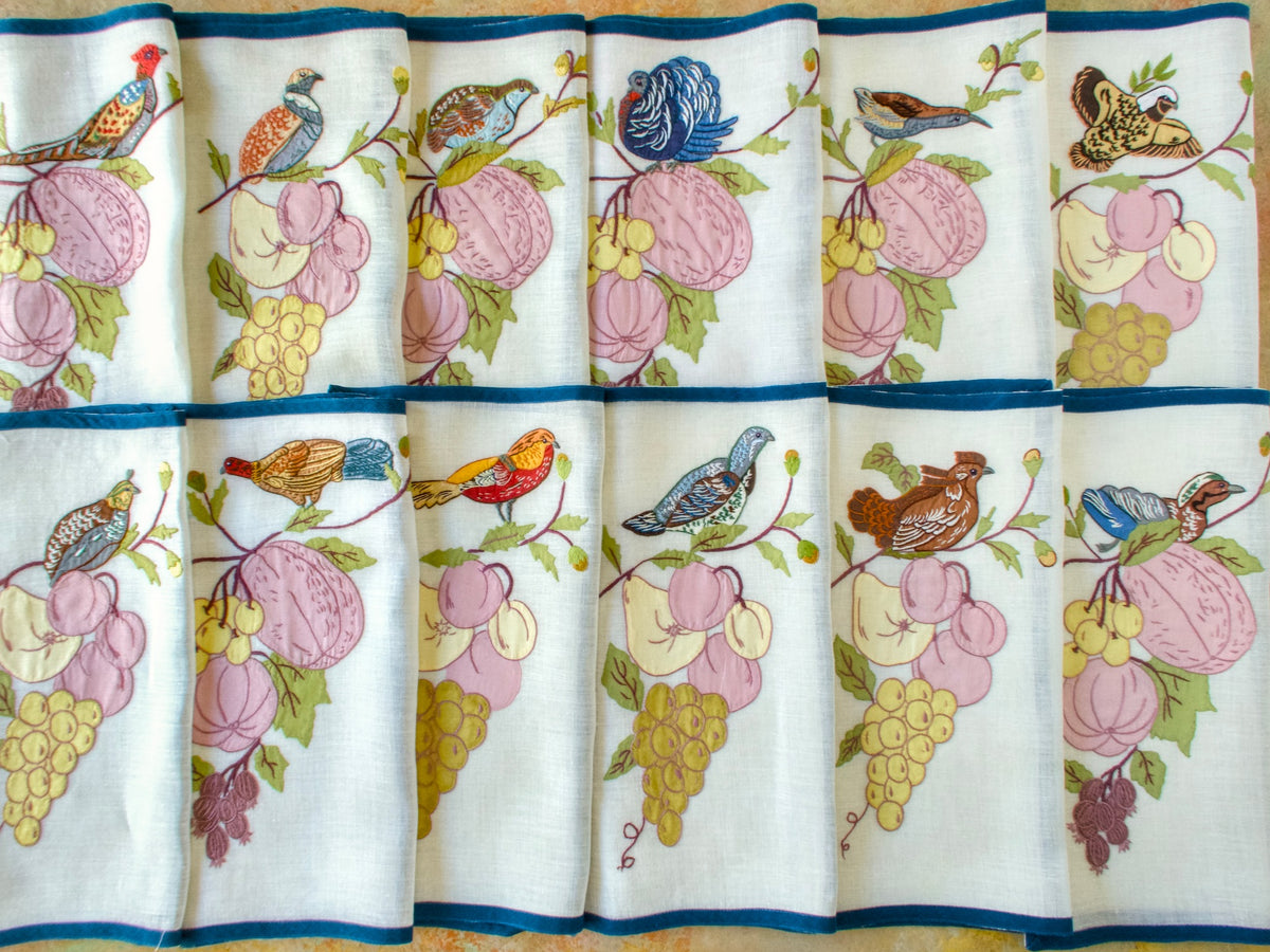 All 12 Italian placemats arranged in two rows, showing the different birds, fruit motifs and blue borders.