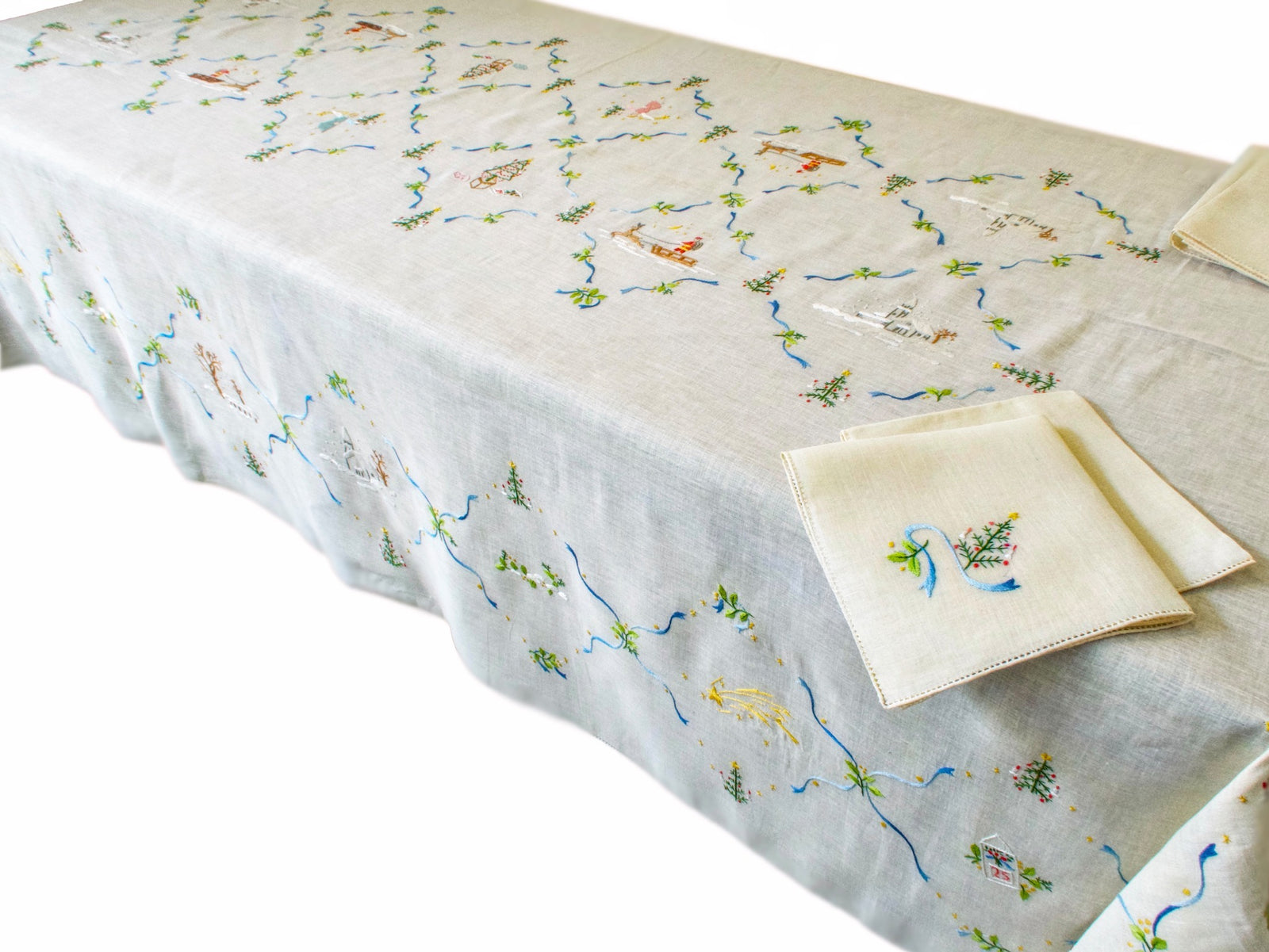 Full view of rectangular vintage linen Christmas tablecloth laid on table, showing scattered embroidered holiday scenes across the surface.