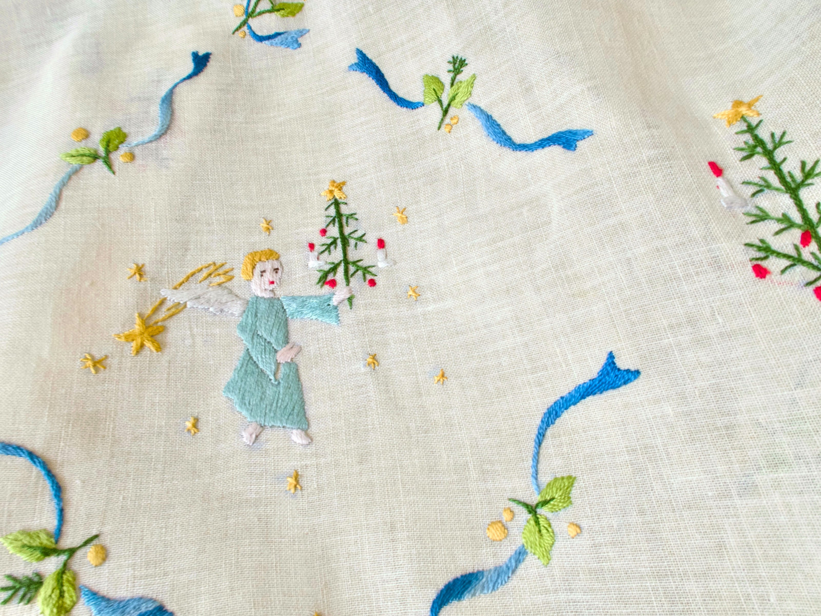 Close-up of embroidered angel motif on linen tablecloth, holding a candle-lit tree.